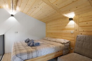 Ein Zimmer mit Holzwandverkleidung, einem Bett, einem Sessel und einer Wandleuchte.