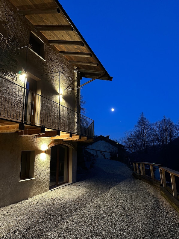 Ein zweistöckiges Gebäude mit einem Balkon, einer Schotterauffahrt und einem klaren Nachthimmel.