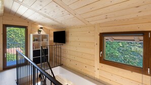 A wooden interior with a staircase, a flat-screen TV, and a window with a view of greenery. - Faunet Apartment with Mountain View, Wi-Fi and Air Conditioning (Bernezzo)