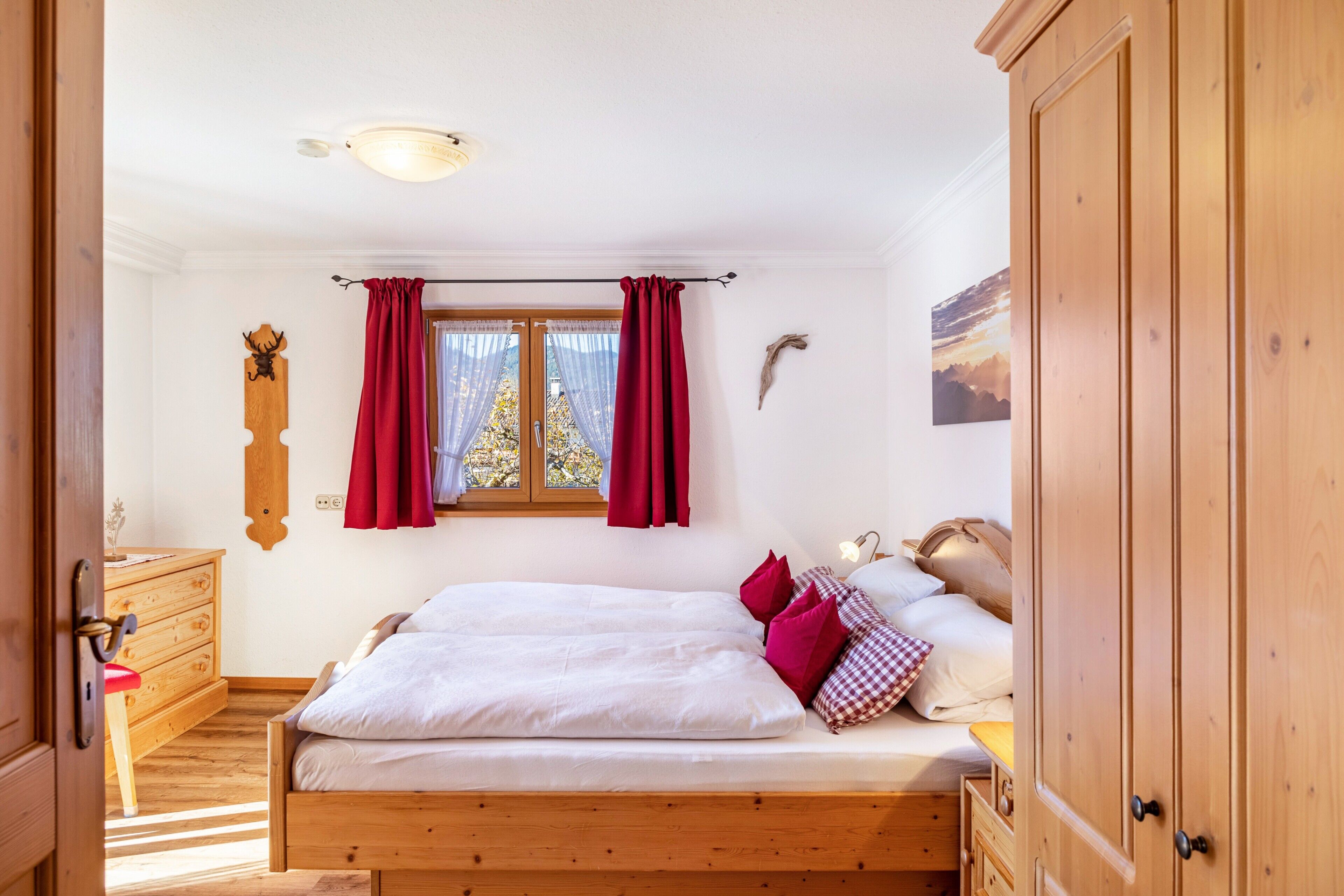 Un dormitorio con cama de madera, cortinas rojas, cómoda de madera y ventana con vistas.