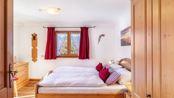 Un dormitorio con cama de madera, cortinas rojas, cómoda de madera y ventana con vistas.