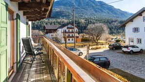 A balcony with a view of a mountain, a parking area with cars, and a building with a traditional design.