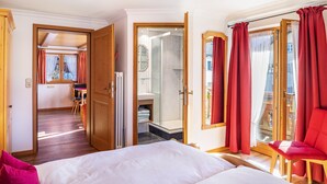A hotel room with a bed, a chair, a bathroom with a shower, and a desk with a chair.