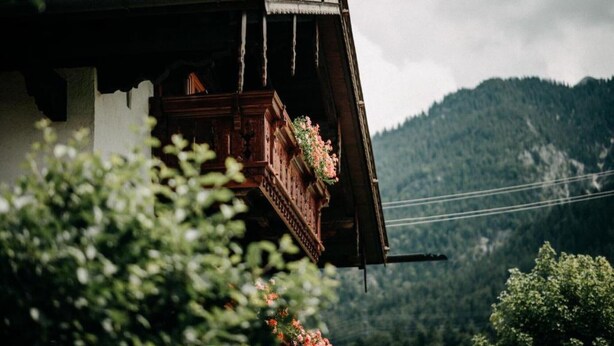A traditional wooden building with a balcony, surrounded by greenery and mountains in the background. - Apartment '2' with Mountain View, Balcony and Wi-Fi (Krün)