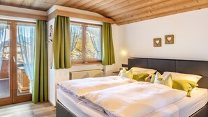 A bedroom with a wooden ceiling, a bed with white bedding, green curtains, and two heart-shaped wall decorations. - Apartment '2' with Mountain View, Balcony and Wi-Fi (Krün)