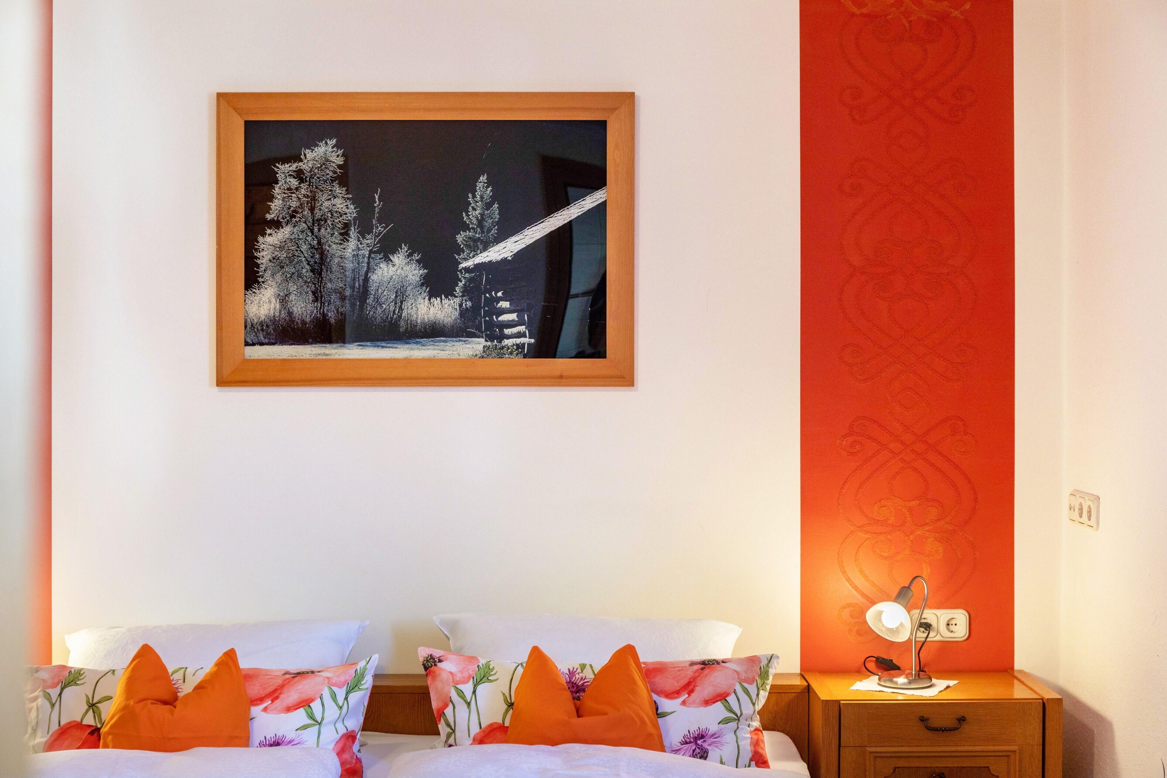 Una camera da letto con un letto, cuscini, un comodino, una lampada e un quadro appeso al muro.