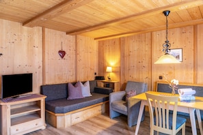 A wooden interior with a sofa, armchair, table, and TV stand.