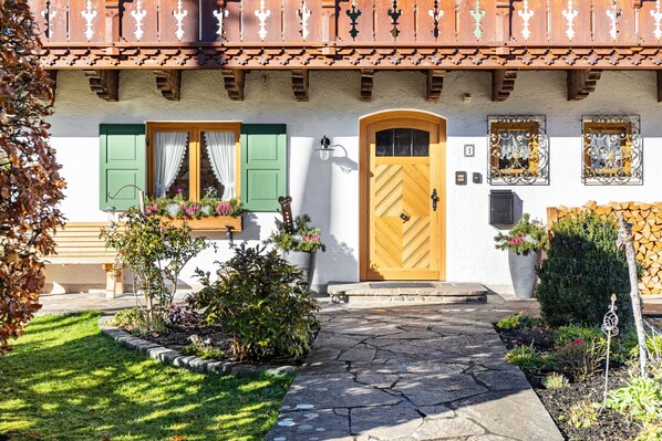 A traditional chalet with a wooden door, green shutters, and a stone pathway leading to the entrance.