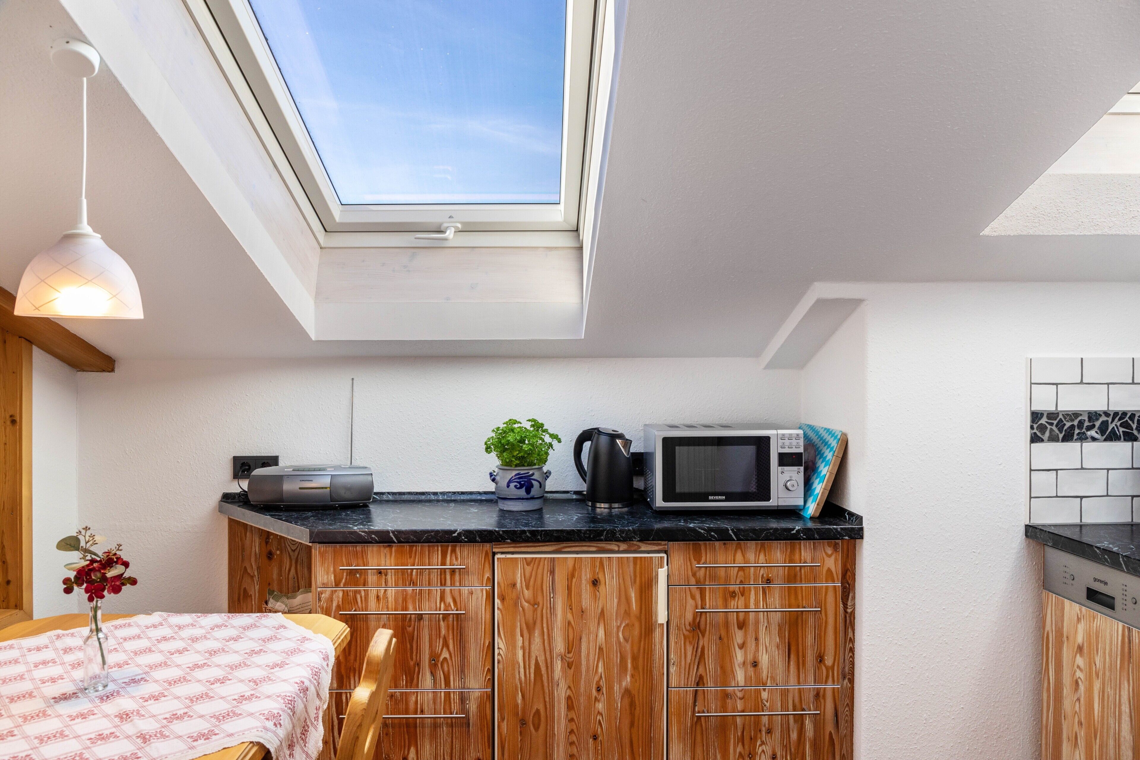 A compact kitchen with a skylight, wooden cabinets, a microwave, and a coffee maker.