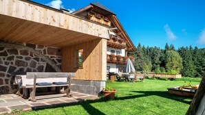 A wooden building with balconies, a stone wall, a bench, and a grassy yard. - Apartment “Kardinerhof Bergwiese” with Mountain View, Shared Garden and Wi-Fi (Ritten)