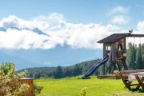 Ein hölzernes Spielhaus mit Rutsche, Picknicktisch und Blick auf Berge.