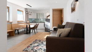 A modern living space with a wooden bench, a sofa, a dining table with chairs, and a kitchen area with a refrigerator and cabinets. - Apartment “Kardinerhof Bergwiese” with Mountain View, Shared Garden and Wi-Fi (Ritten)