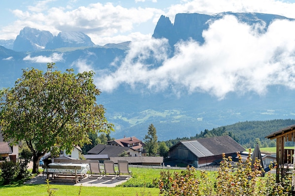 A mountain village with traditional houses, a large tree, and a view of the mountains.