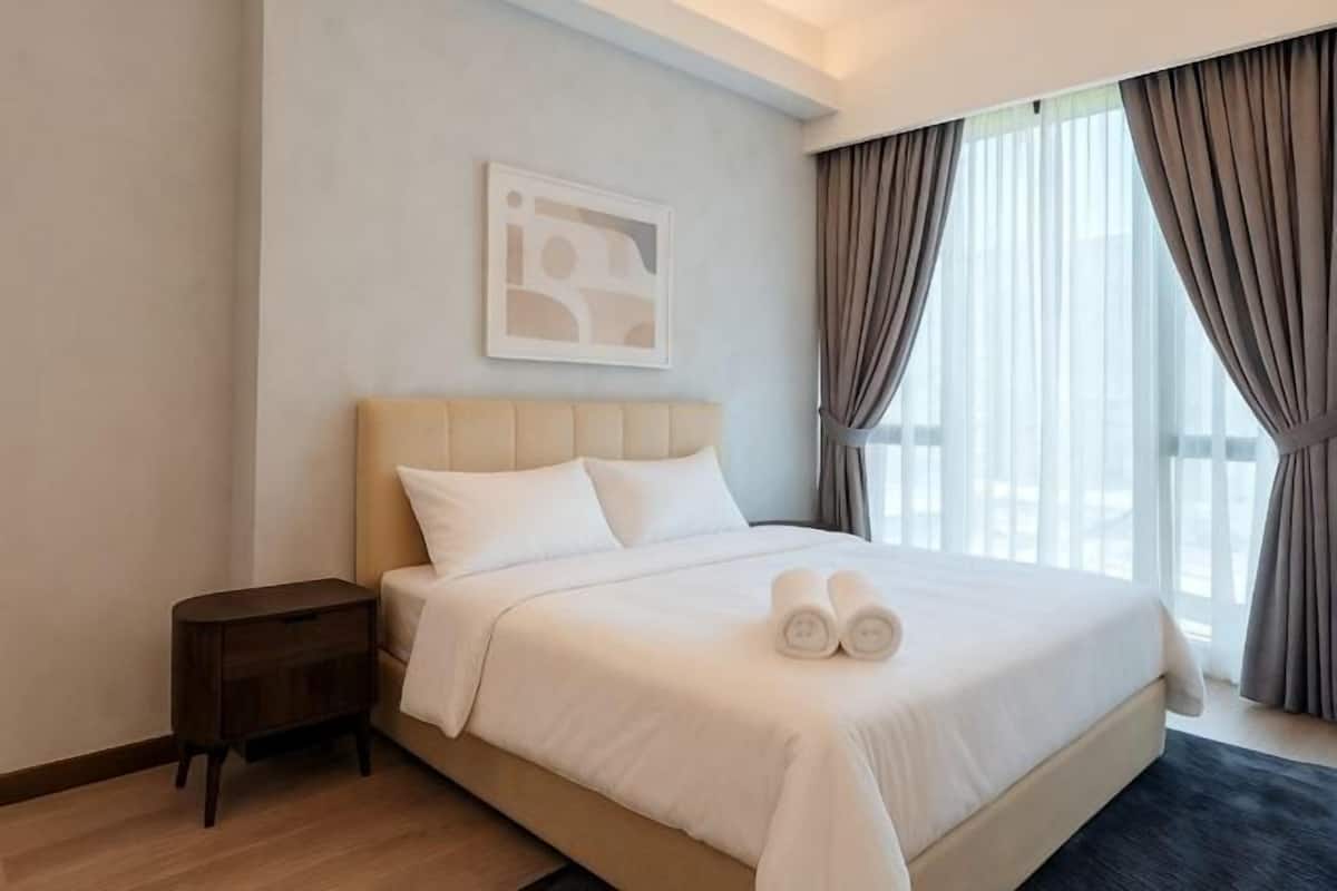 A neatly made bed with white linens, a headboard, and a small bedside table.