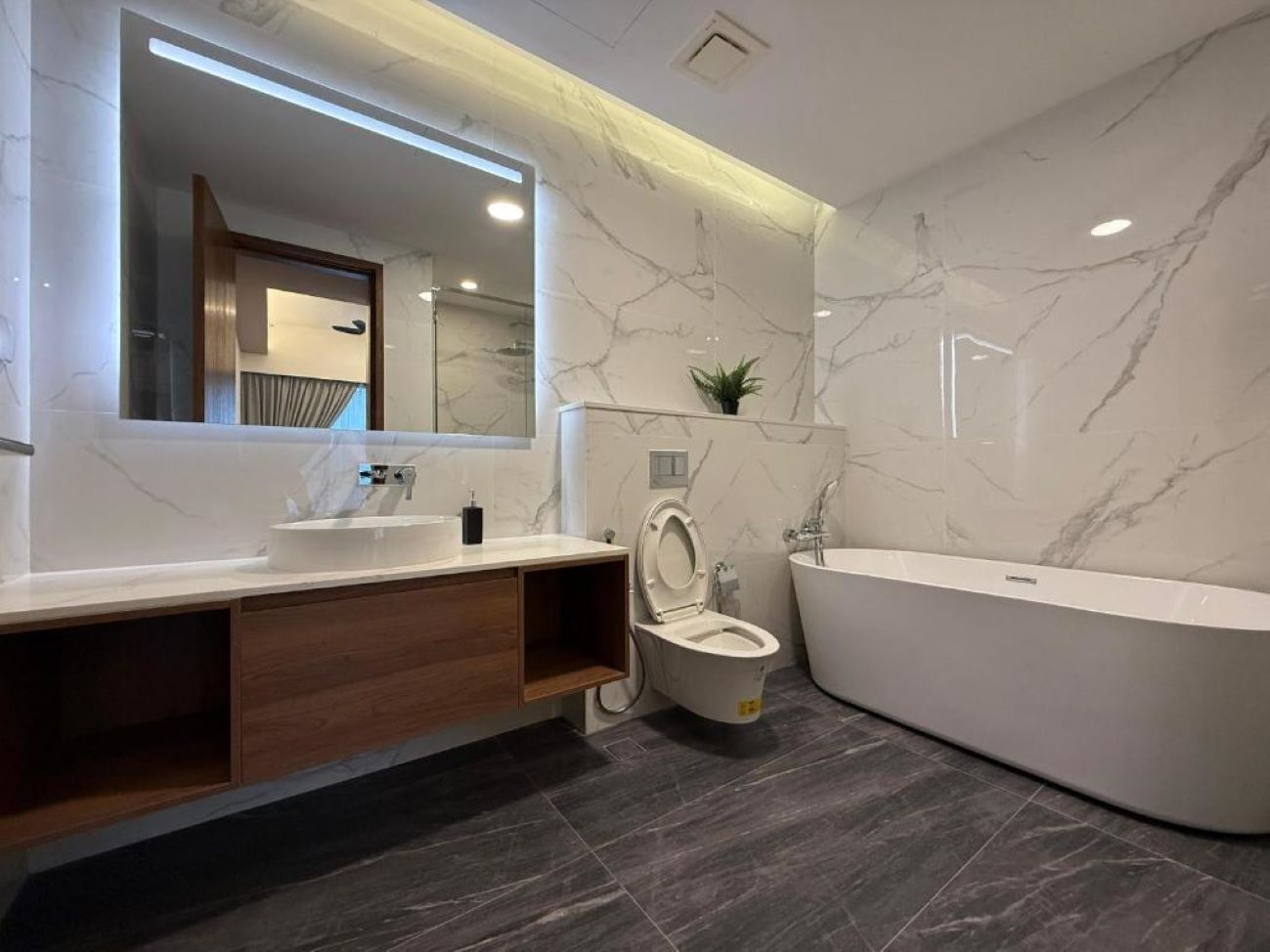 A modern bathroom with a marble vanity, a toilet, and a freestanding bathtub.