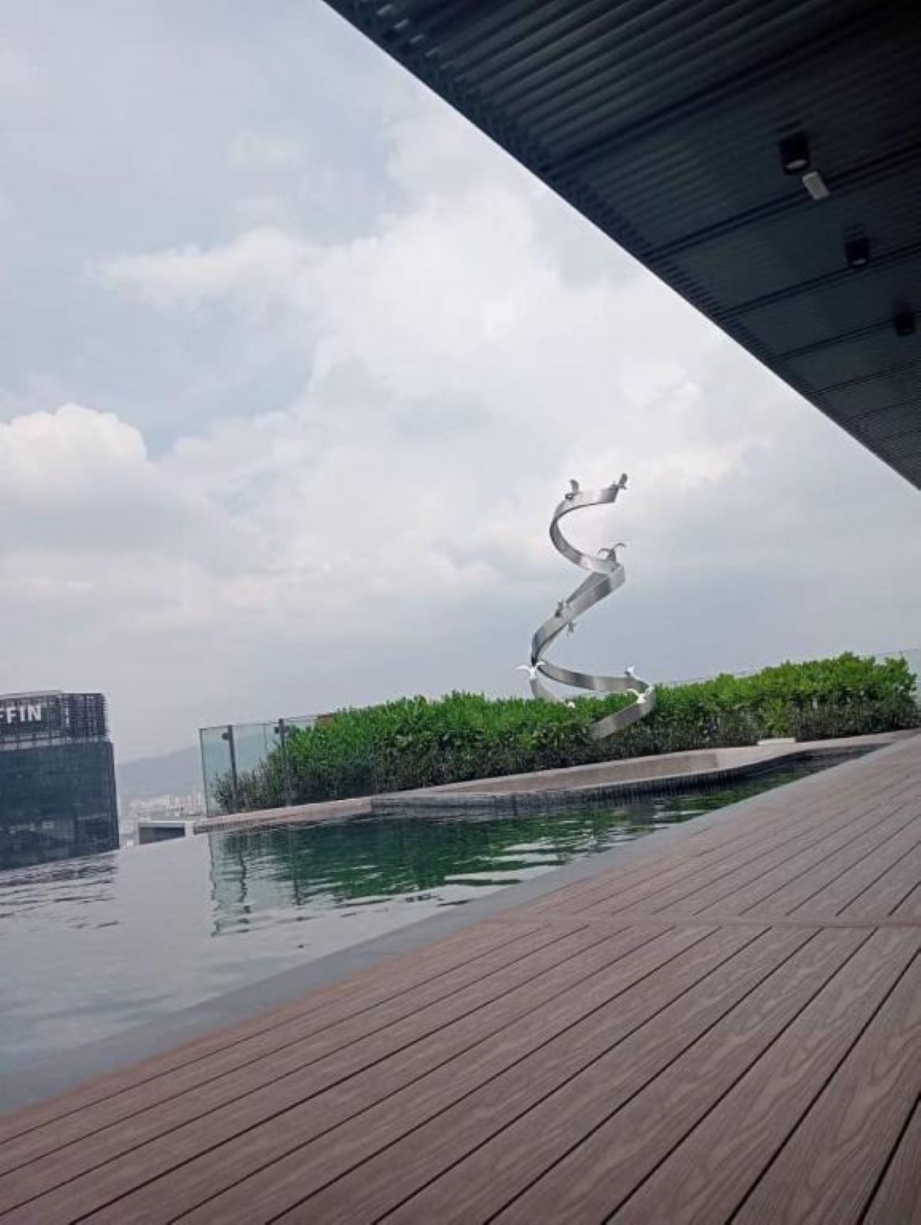 A rooftop pool area with a metal sculpture, wooden deck, and a view of a building labeled "FIN".