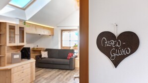 A heart-shaped sign with text, a wooden cabinet, a gray sofa, and a skylight. - Apartment 'Alpenglühn' with Dolomite Views, Balcony and Wi-Fi (Ritten)