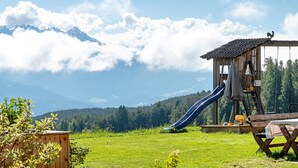 A wooden playhouse with a slide, a picnic table, and a view of mountains. - Apartment 'Alpenglühn' with Dolomite Views, Balcony and Wi-Fi (Ritten)