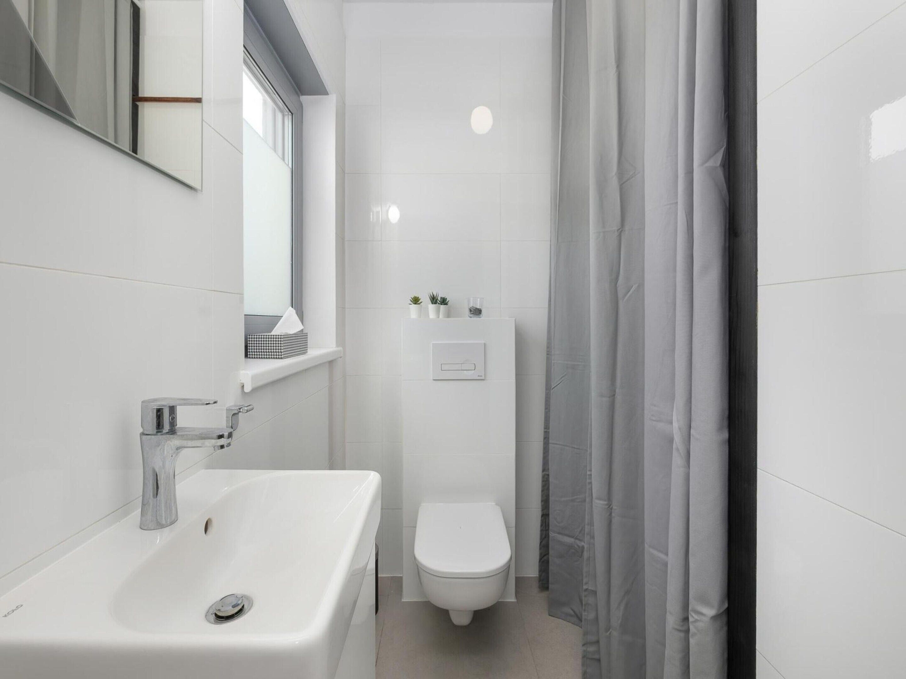 Un bagno moderno con un lavandino bianco, un water e una tenda da doccia.