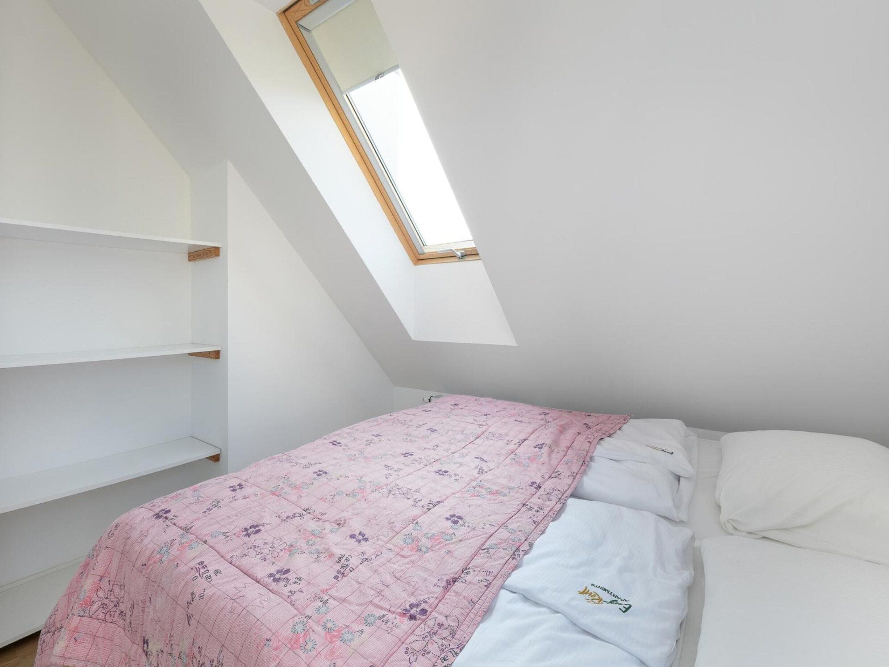 Ein Schlafzimmer mit schrägem Dach, einem Oberlicht, einem Bett mit floralem Überwurf und weißer Bettwäsche.