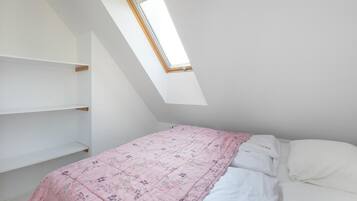 Ein Schlafzimmer mit schrägem Dach, einem Oberlicht, einem Bett mit floralem Überwurf und weißer Bettwäsche.