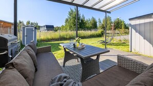 An outdoor patio with a covered seating area, a grill, and a table with a basket and glassware.
