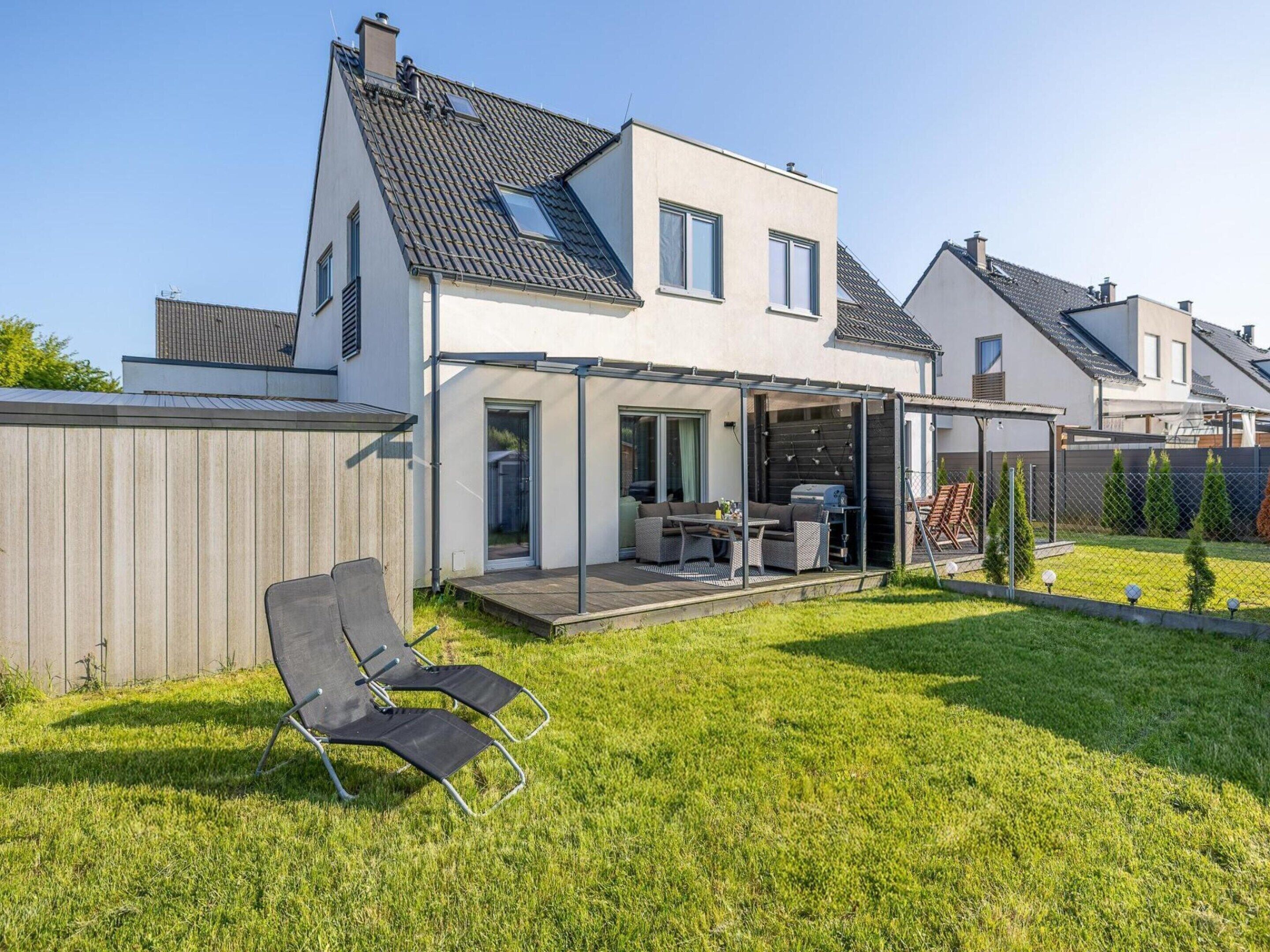 Et moderne hus med to etager, en overdækket terrasse, græsplæne og et træhegn.