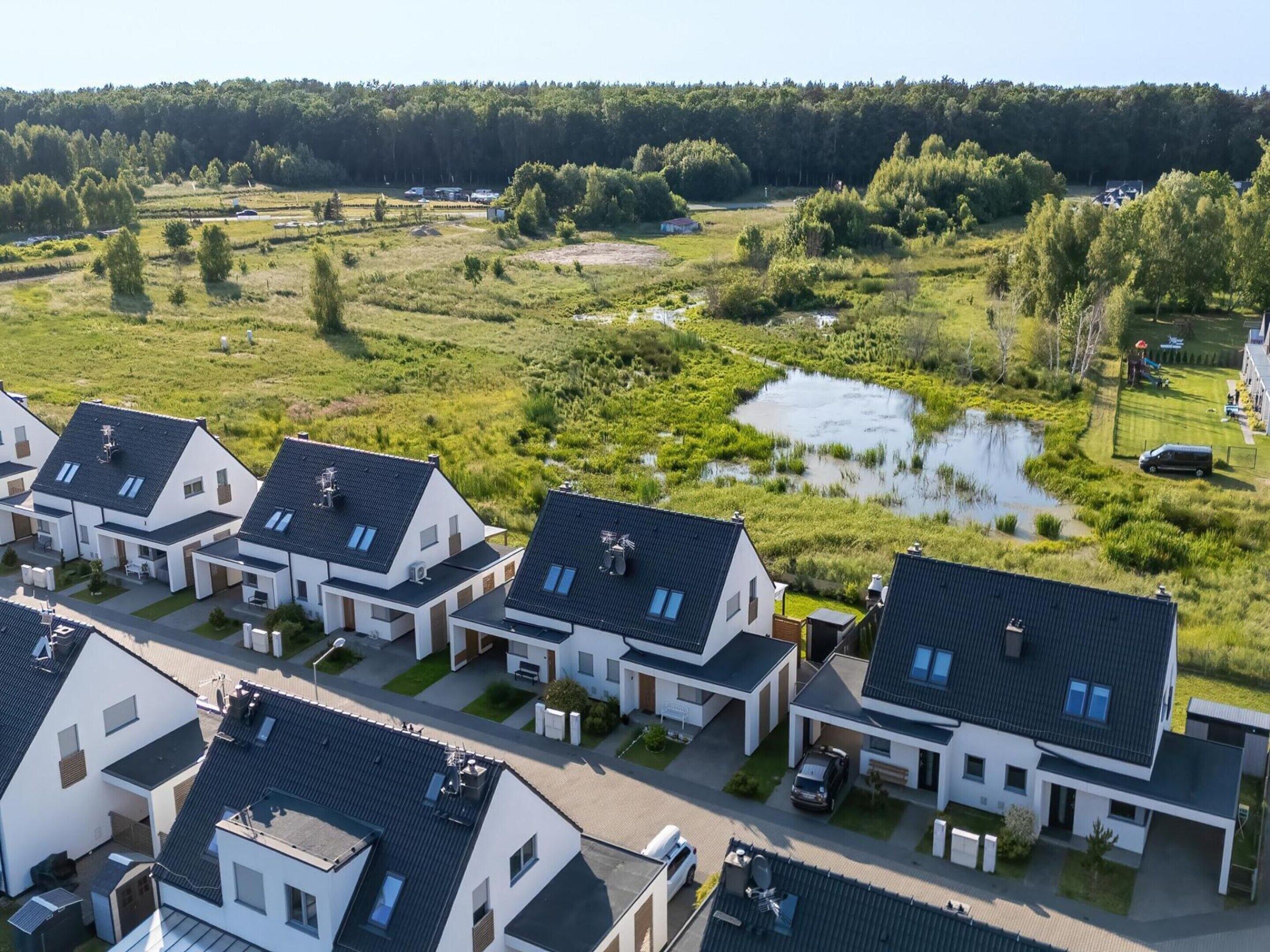A residential area with modern houses, a small pond, and a forested background.