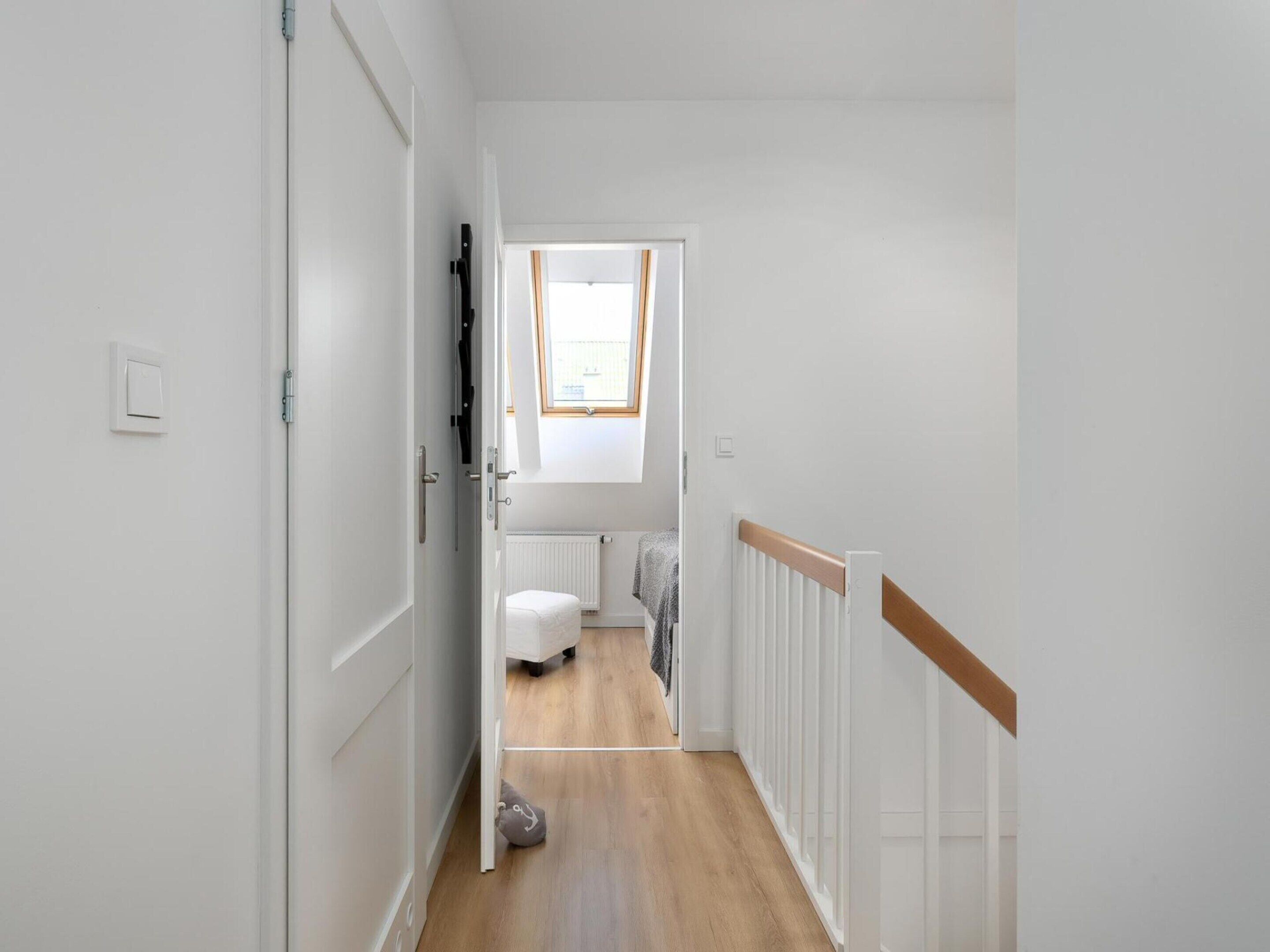 Un couloir étroit aux murs blancs, doté d’un plancher en bois et d’une porte blanche sur le côté gauche.