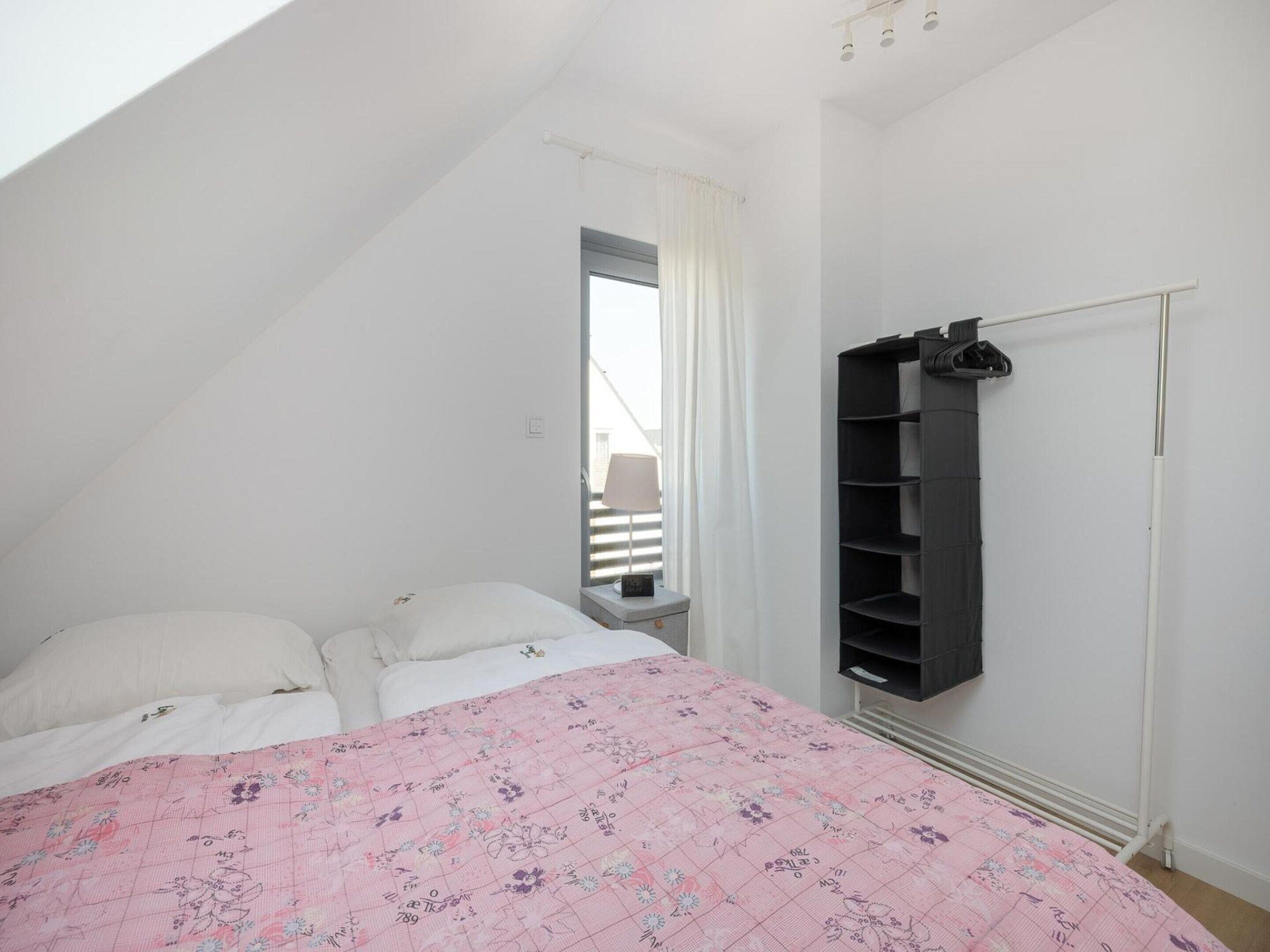 A bedroom with a sloped ceiling, a bed with a floral bedspread, a wardrobe, and a window with curtains.