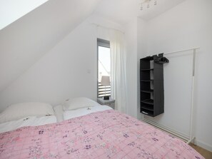 Un dormitorio con techo inclinado, cama con colcha floral, armario y ventana con cortinas.
