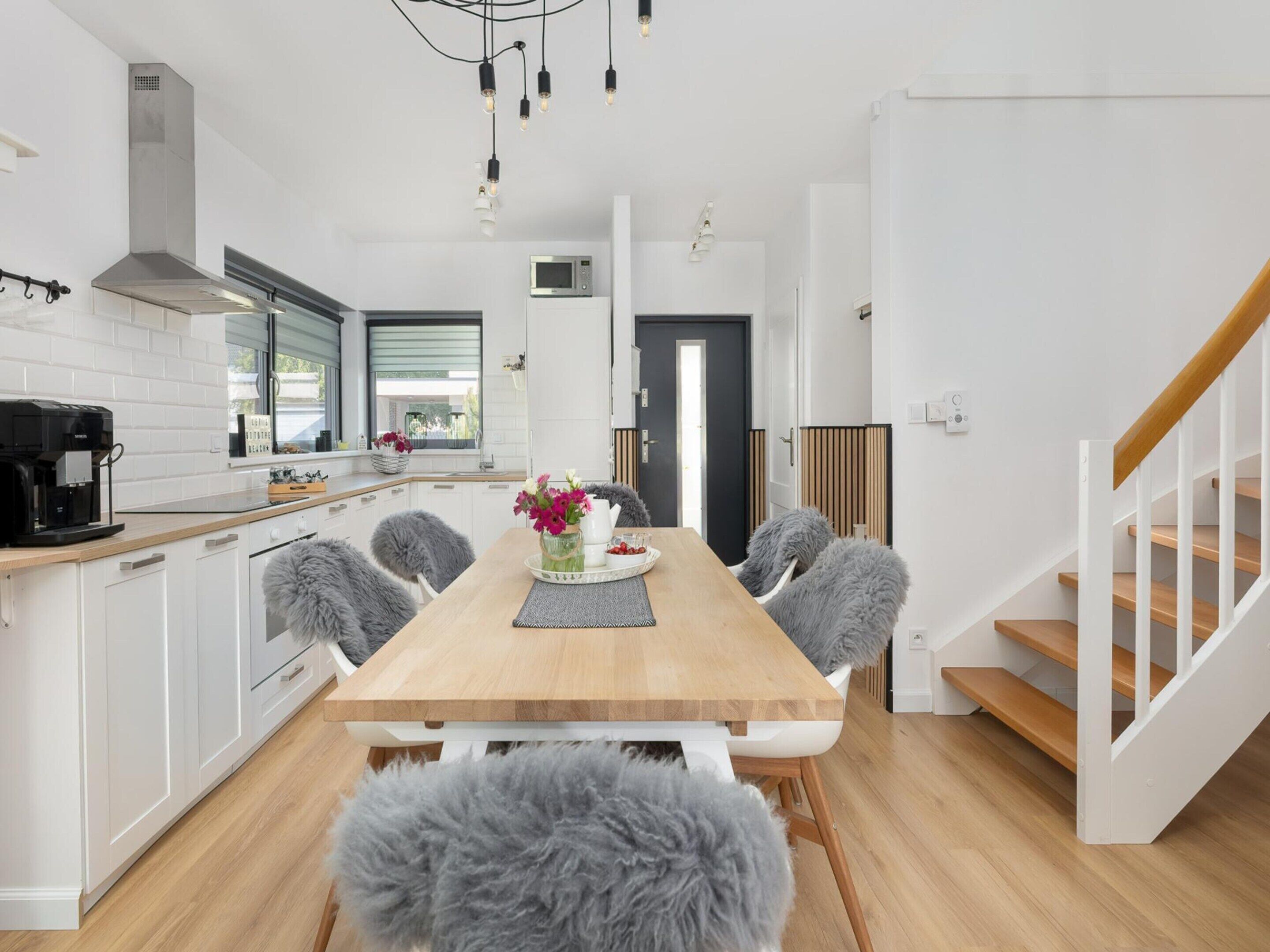 Una cocina moderna con muebles blancos, una mesa de comedor de madera y una escalera.