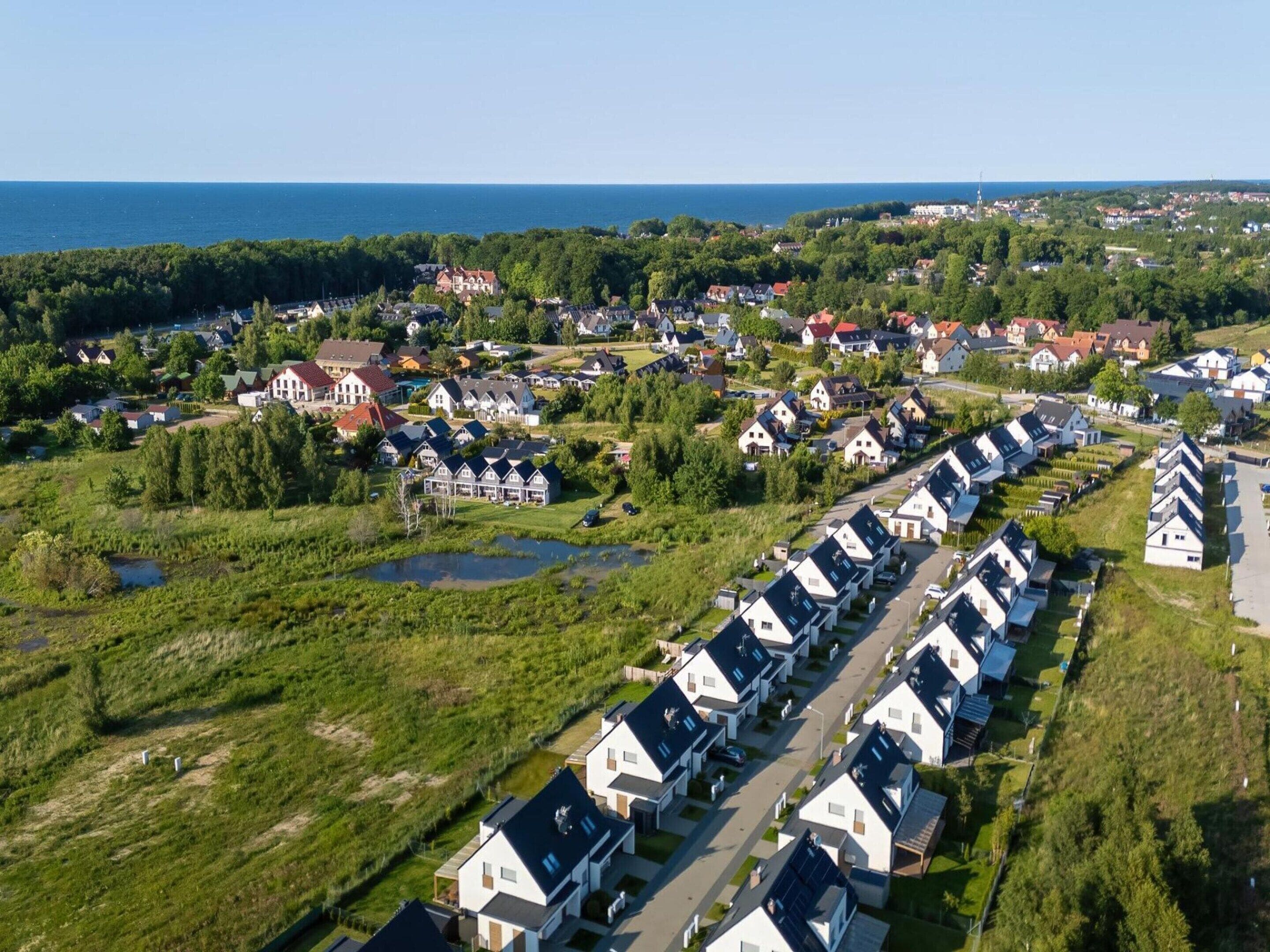 A residential area with houses arranged in rows, a body of water, and a coastline in the background.