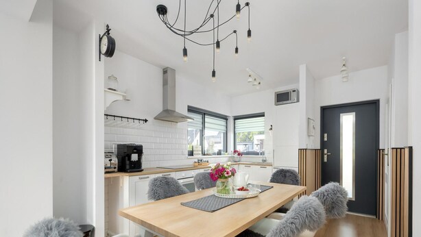 A modern kitchen with a dining area, white cabinetry, a coffee machine, and a black-framed clock.