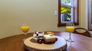 Een houten eettafel met een rond houten bord waarop een gelaagde dessert en twee glazen sinaasappelsap staan.