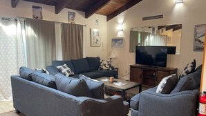 Een woonkamer met een zithoek, een salontafel, een televisie en een open haard.
