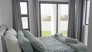 A modern bedroom with a bed, grey curtains, and a view of the outdoors.