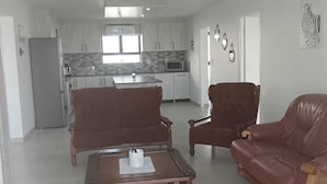 A spacious living area with a kitchen in the background, featuring a dining table and two sofas.