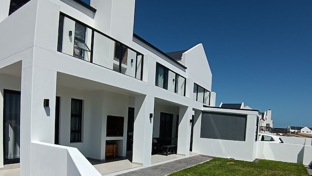 A modern white building with a flat roof, large windows, and a paved driveway leading to a grassy area.