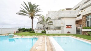 A modern building with a swimming pool, palm trees, and a well-maintained lawn. - Luxury Apartment with Private Pool on Huge Terrace- Ideal for Families and Expats (Las Palmas de Gran Canaria)