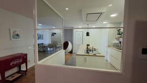 A modern kitchen with a central island, a refrigerator, and a dining area with a red Coca-Cola cooler. - Luxury Apartment with Private Pool on Huge Terrace- Ideal for Families and Expats (Las Palmas de Gran Canaria)