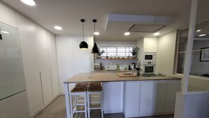 A modern kitchen with white cabinetry, a wooden countertop, and a central island with stools. - Luxury Apartment with Private Pool on Huge Terrace- Ideal for Families and Expats (Las Palmas de Gran Canaria)