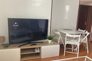 A modern living room with a flat-screen TV, a small plant, and a white dining table with chairs.