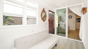 Una habitación con un sofá blanco, un espejo grande y un ventanal corredero que da a otra estancia.