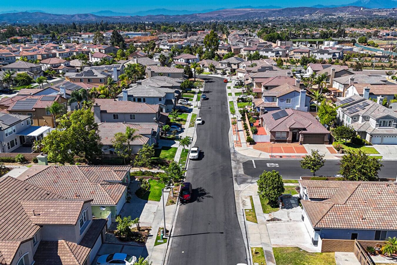 Une rue résidentielle bordée de maisons, un ciel dégagé et des montagnes à l’horizon.