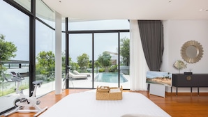 Ein modernes Schlafzimmer mit einem großen Bett, Blick auf einen Swimmingpool und einem Fitnessrad.