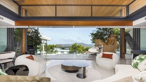 Un salon moderne doté d’une grande baie vitrée, de canapés blancs, d’une table basse ronde et offrant une vue sur les montagnes.