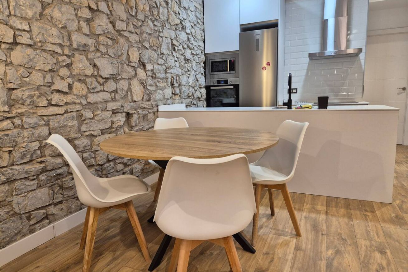 A modern kitchen with a stone wall, a round wooden table, and four white chairs.