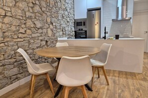 Eine moderne Küche mit einer Steinwand, einem runden Holztisch und vier weißen Stühlen.