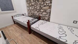 Una habitación con dos camas individuales, una pared de piedra, una ventana y suelo de madera.